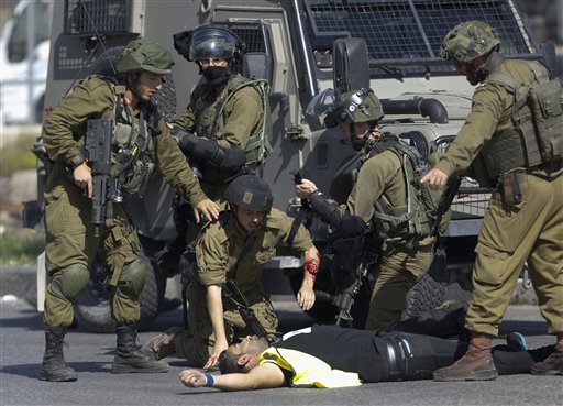 A wounded Israeli soldier kneels over the body of a Palestinian who stabbed him during clashes in Hebron, West Bank Friday, Oct. 16, 2015. The Palestinian man wearing a yellow "press" vest and a T-shirt identifying him as journalist stabbed and wounded an Israeli soldier in the West Bank city of Hebron on Friday before being shot dead by troops, the latest in a monthlong spate of attacks. (AP Photo/Nasser Shiyoukhi)