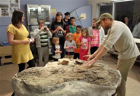 Tom Suazo, right, a fossil predator with the New Mexico Museum of Natural History and Science, tells a group of children about the museum's latest find as discover Amanda Cantrell, left, listens during a public unveiling in Albuquerque, N.M., on Thursday, Nov. 5, 2015. The baby Pentaceratops skull on display in the museum's preparation room is the first to ever be discovered. (AP Photo/Susan Montoya Bryan)