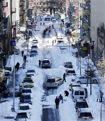 People clear snow from parked cars on Henry Street in the Chinatown neighborhood in New York on Sunday, Jan. 24, 2016. Millions of Americans began digging out Sunday from a mammoth blizzard that set a new single-day snowfall record in Washington and New York City. (AP Photo/Peter Morgan)
