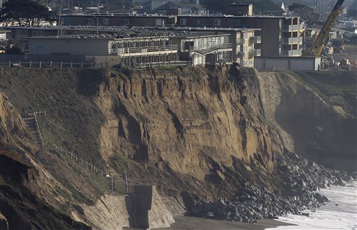 FILE - In this Jan. 27, 2016 file photo, boulders shore up an eroding cliff below an apartment complex that residents were forced to evacuate, at top left, in Pacifica, Calif. Living with the Pacific Ocean as your backyard has its benefits. But the crumbling ocean cliffs have forced dozens to move quickly and at a high cost. (AP Photo/Jeff Chiu, file)