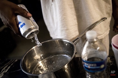 Flint resident Lorraine Jones pours canned water into a pot in preparation for boiling to cook on Tuesday, Jan. 19, 2016, at River Park Apartments in Flint, Mich. After weeks without water being distributed, the residents are finally getting bottled water delivered to their doorsteps for the first time Tuesday as four Flint Housing Commission workers shuttled cases of water throughout the community. (Jake May/The Flint Journal-MLive.com via AP)