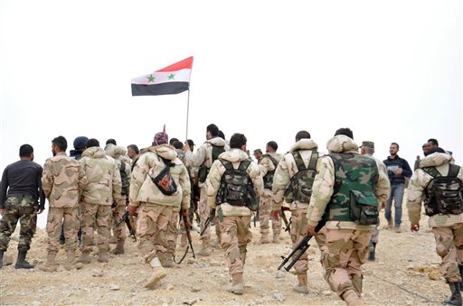 In this photo released by the Syrian official news agency SANA, Syrian soldiers gather around a Syrian national flag in Palmyra, Syria, Sunday, March 27, 2016. Syrian state media and an opposition monitoring group say government forces backed by Russian airstrikes have driven Islamic State fighters from the historic central town of Palmyra, held by the extremists since May. (SANA via AP)