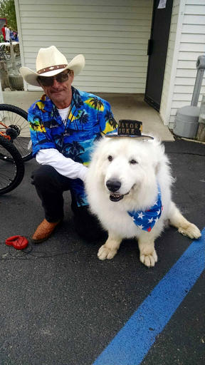 This Saturday, Aug. 20, 2016 photo provided by Karen Nelson shows owner, Dave Rick, with his dog, Duke, a 9-year-old Great Pyrenees, that won a third one-year term as honorary mayor of Cormorant Township, Minn. The big, shaggy white dog was overwhelmingly re-elected at the sixth annual Cormorant Daze Festival. (Deb Rick via AP)